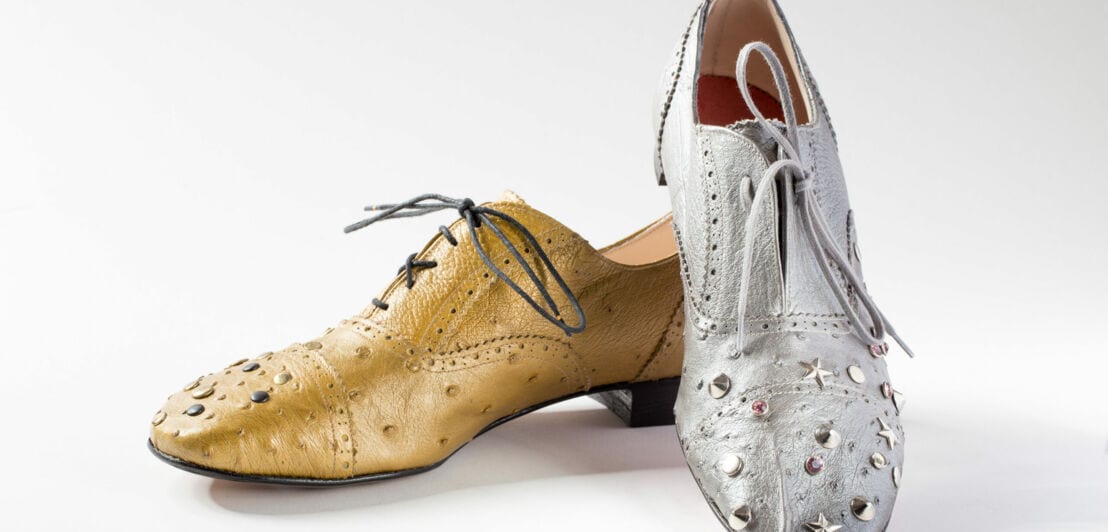 Ein goldener und ein silberner Schuh mit Nieten verziert vor einem weißen Hintergrund