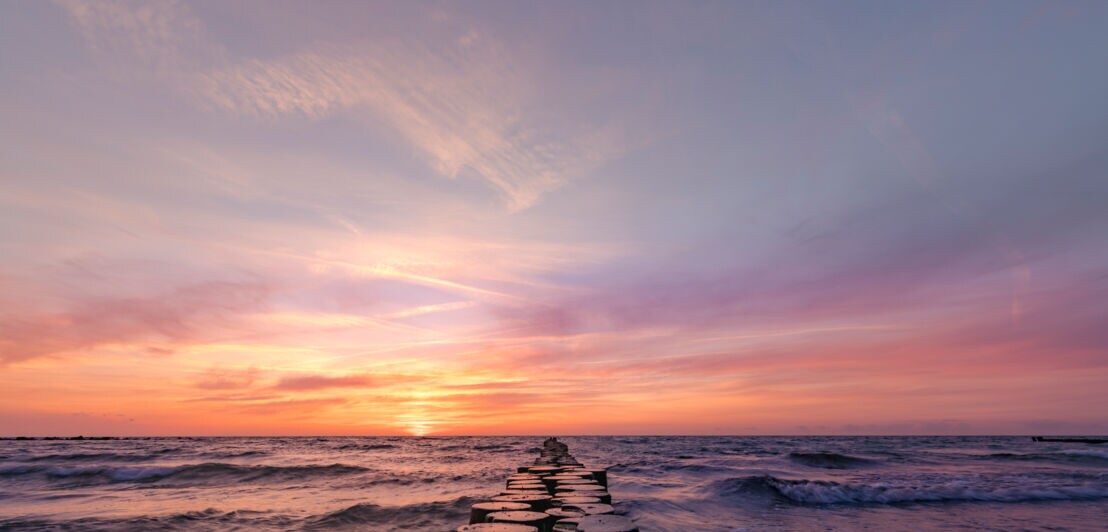 Ein Sonnenuntergang über dem Meer, in dem ein Holzsteg ins Wasser führt