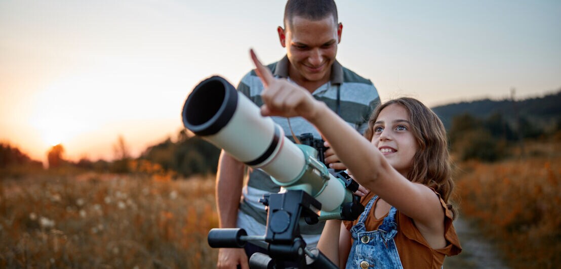 Ein Erwachsener und ein Mädchen mit einem Teleskop in der Wildnis.