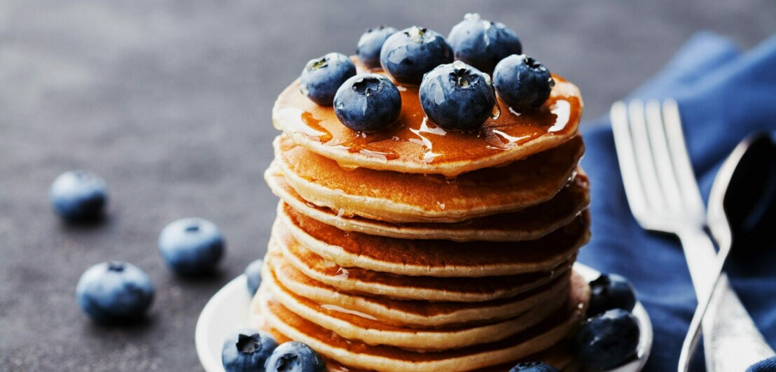 Nahaufnahme von geschichteten Pancakes auf Teller, getoppt mit Blaubeeren und Syrup