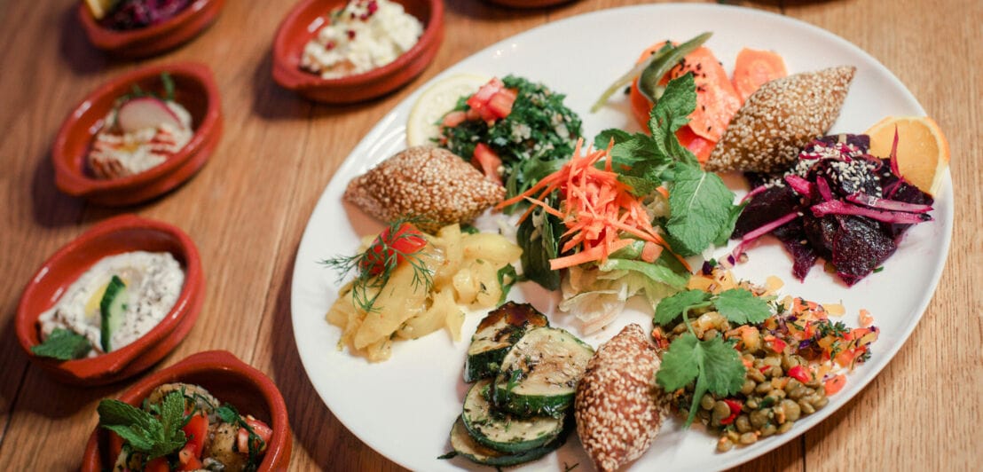 Ein großer Teller mit gemischten vegetarischen Speisen, umgeben von kleinen gefüllten Schalen auf Holztisch
