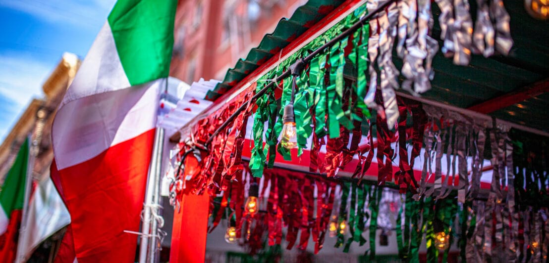 Nahaufnahme von Girlanden und Fahnen in den italienischen Nationalfarben vor einer Hausfassade