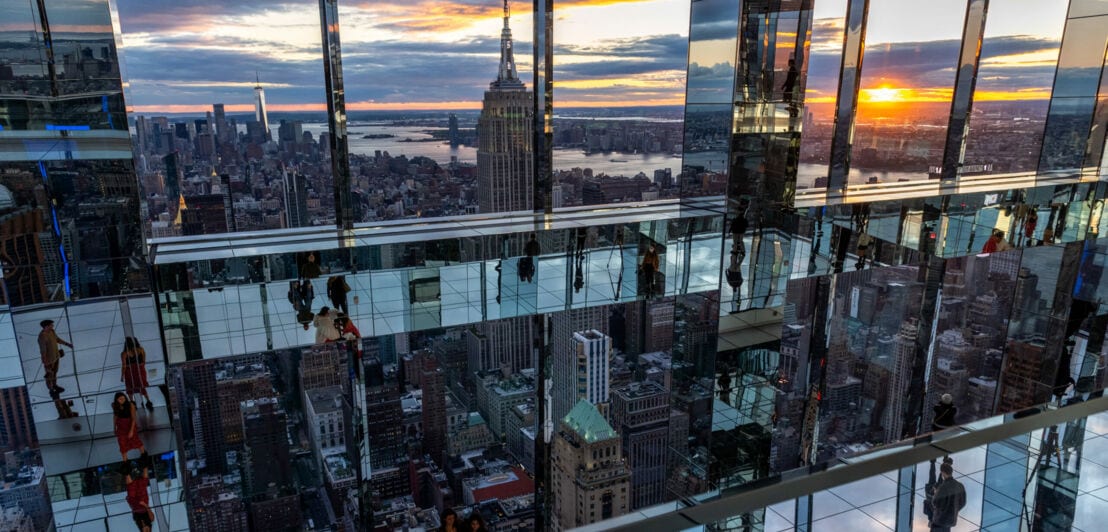 Besucher laufen über eine gläserne Aussichtsplattform in Manhattan mit Blick auf das Empire State Building