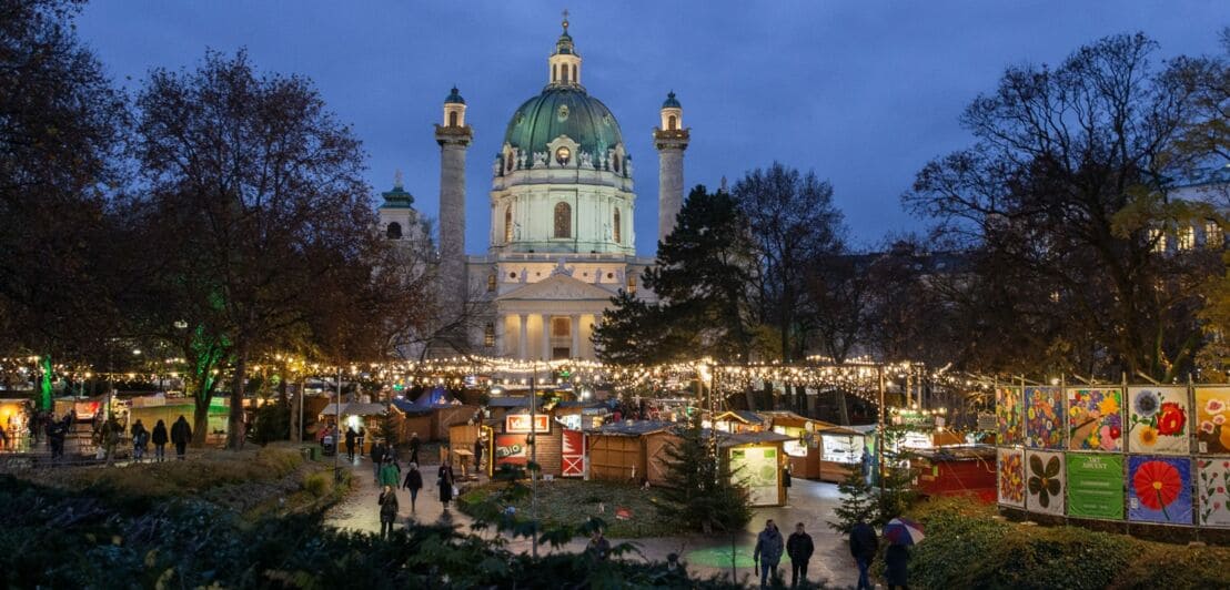 Beleuchteter Weihnachtsmarkt mit Verkaufsständen vor der Karlskirche in Wien bei Nacht