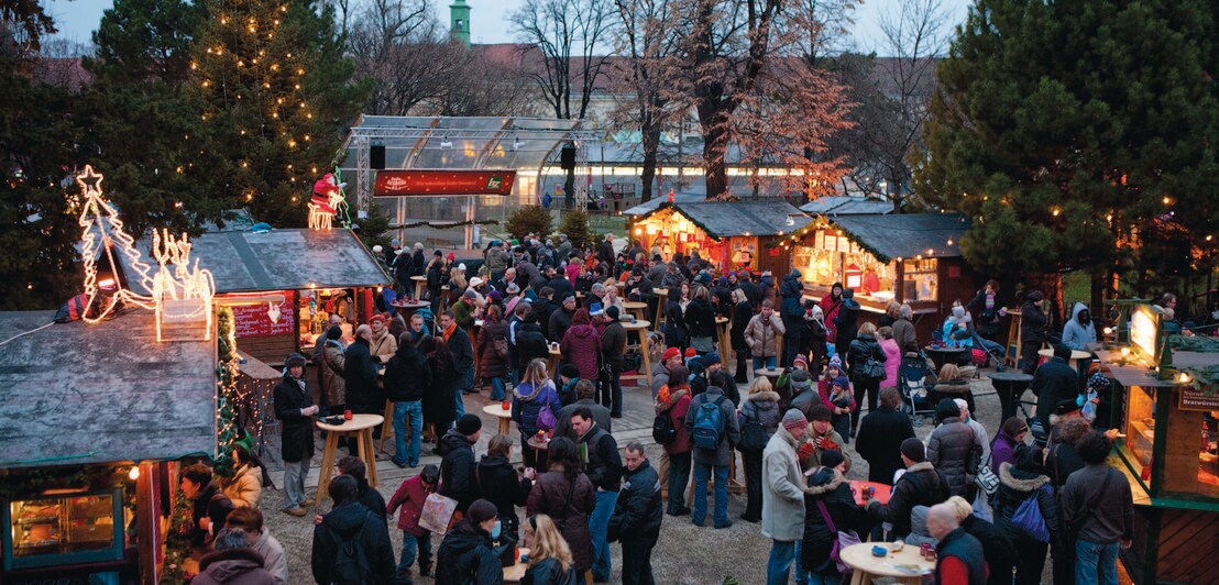 Weihnachtsmarkt mit Menschenansammlung umgeben von Verkaufsständen in der Dämmerung