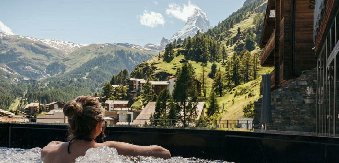 Rückansicht einer Frau, die in einem Whirlpool im Freien auf ein Bergpanorama mit Matterhorn blickt