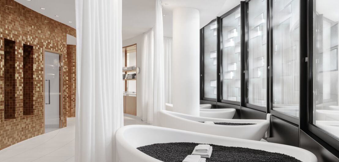 Innenraumaufnahme eines hellen Spas mit ovalen Badewannen, die mit schwarzen Steinen gefüllt sind