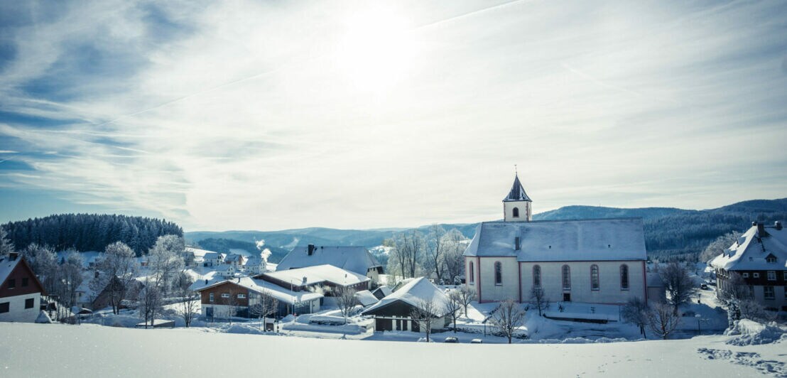Ein eingeschneites Dorf im Sonnenschein, im Hintergrund Berge