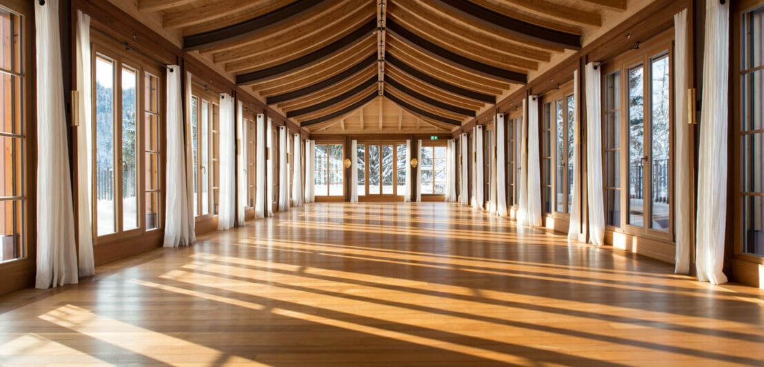 Ein großer, lichtdurchfluteter Raum aus Holz mit bodentiefen Fenstern und einem fernöstlichen Walmdach