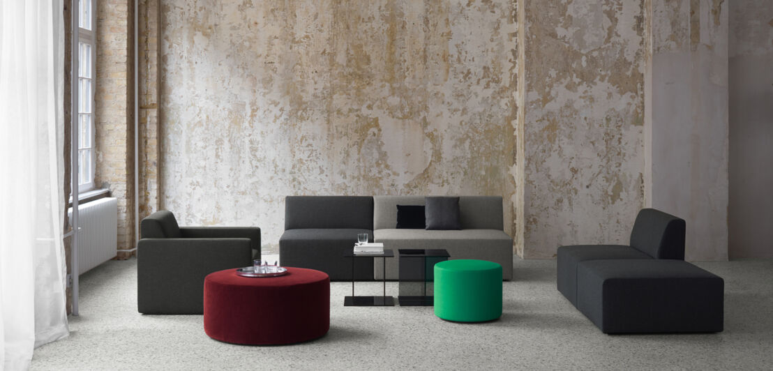 Sitzgruppe aus minimalistischen Polstermöbeln und Beistelltischen in einem großen Raum vor Betonwand