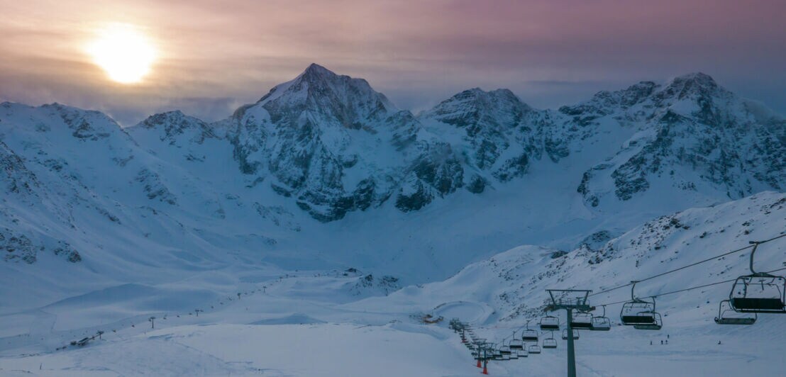 Seilbahn, Schnee und Berge. Im Hintergrund ein Sonnenuntergang