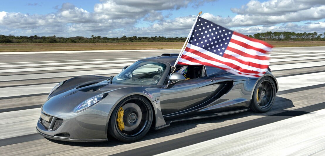 Der Hennessey Venom GT auf einer Rennstrecke, aus dem Fenster wird eine amerikanische Flagge gehalten.