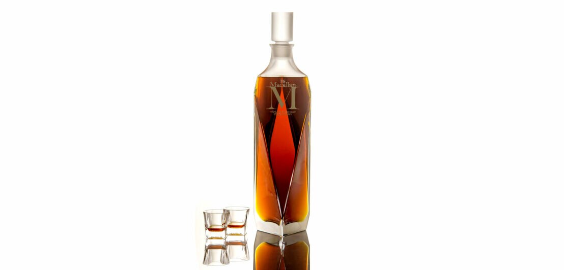 In Diamantenform geschliffener Dekanter mit Whisky der Marke Macallan M, daneben zwei kleine Whisky-Gläser