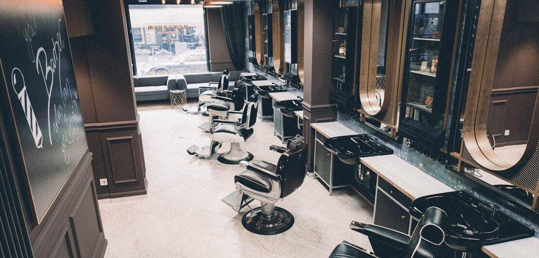 Das elegante Interieur eines Barbershops mit Friseursesseln, Waschbecken, schokoladenfarbenen Wänden und Messingelementen