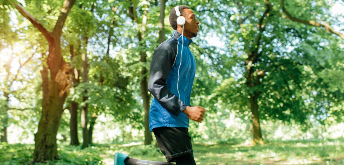 Mann mit Kopfhörern joggt durch den Park