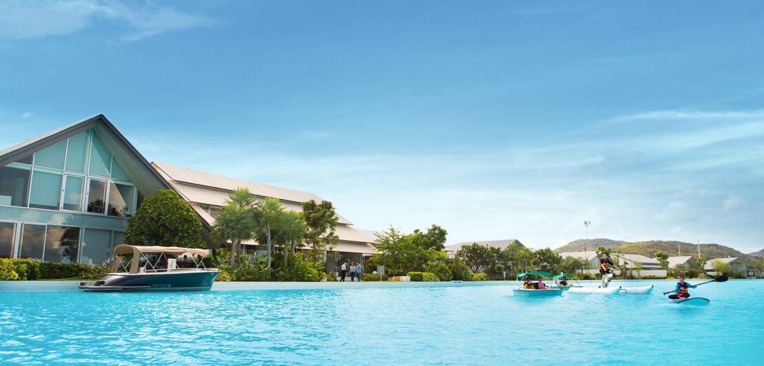 Ein klarer, meeresartiger Pool mit Thailand-typischen Booten vor dem Hintergrund luxuriöser Villen und Hügel