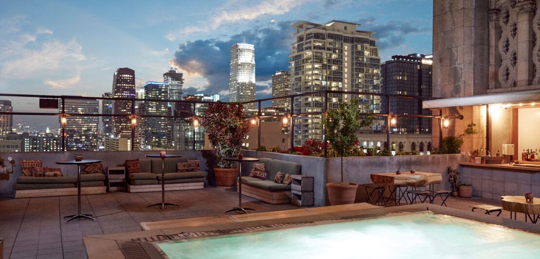 Dachterrasse mit Pool, Bar und Sitzmöglichkeiten mit Blick auf die Innenstadt von Los Angeles am Abend