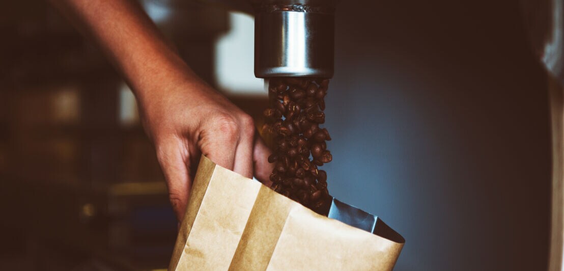 Nahaufnahme einer Hand, die Kaffeebohnen in eine Verpackung abfüllt