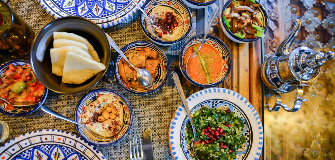 Eine Vielzahl an unterschiedlichen Vorspeisen ist auf orientalischen Tellern angerichtet.