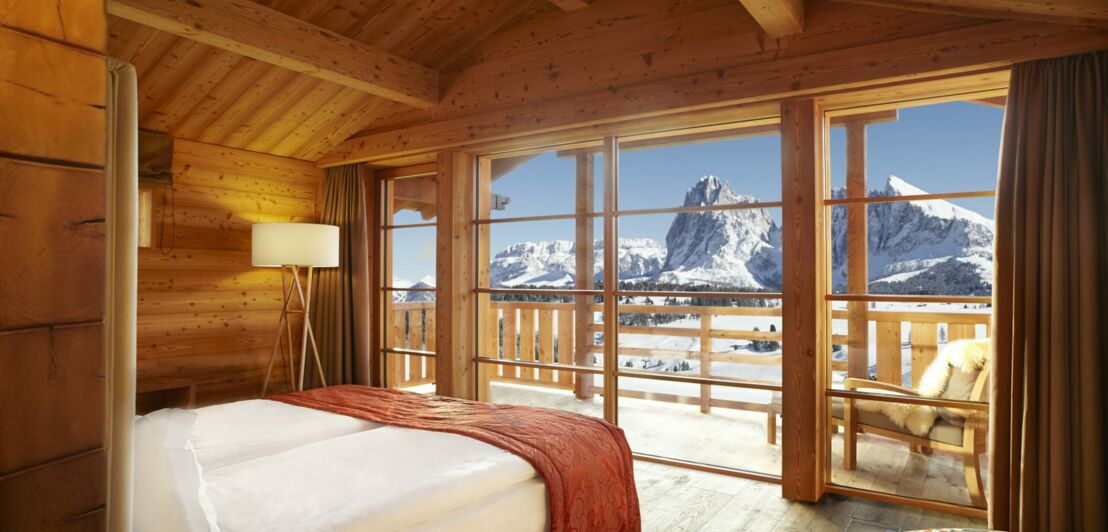 Innenansicht eines Hotelzimmers mit großer Fensterfront, im Hintergrund schneebedeckte Berge
