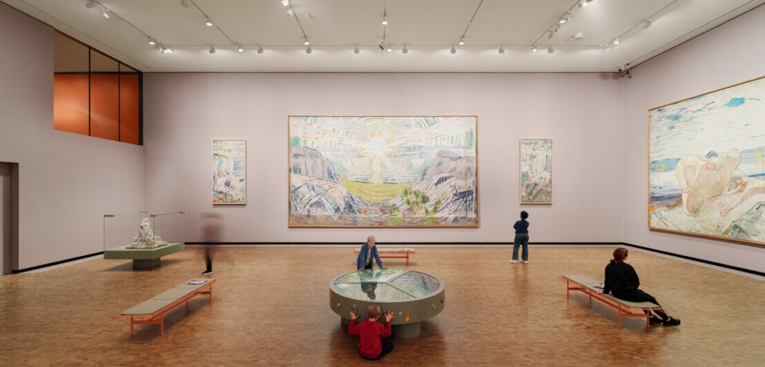 In einem großen Museumssaal betrachten einige Menschen Kunstwerke, darunter zwei großformatige Gemälde