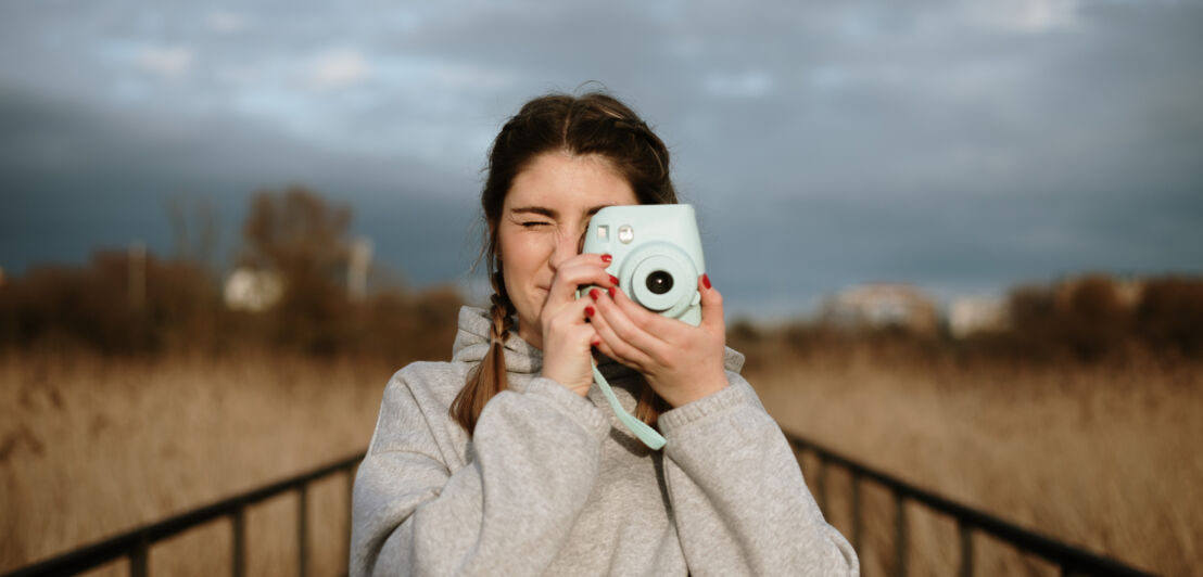 Eine junge Frau in einem Feld fotografiert mit einer Sofortbildkamera