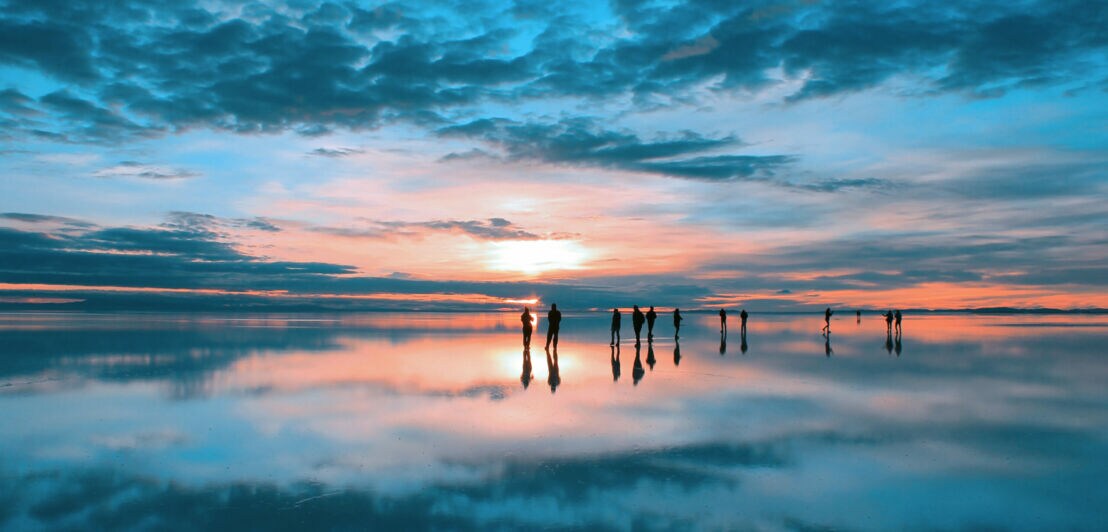 Eine Gruppe von Personen steht bei Sonnenaufgang auf einer Wasserfläche