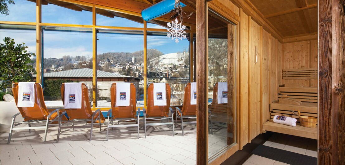 Saunabereich mit Liegestühlen vor einem Panoramafenster mit Blick in die verschneite Berglandschaft