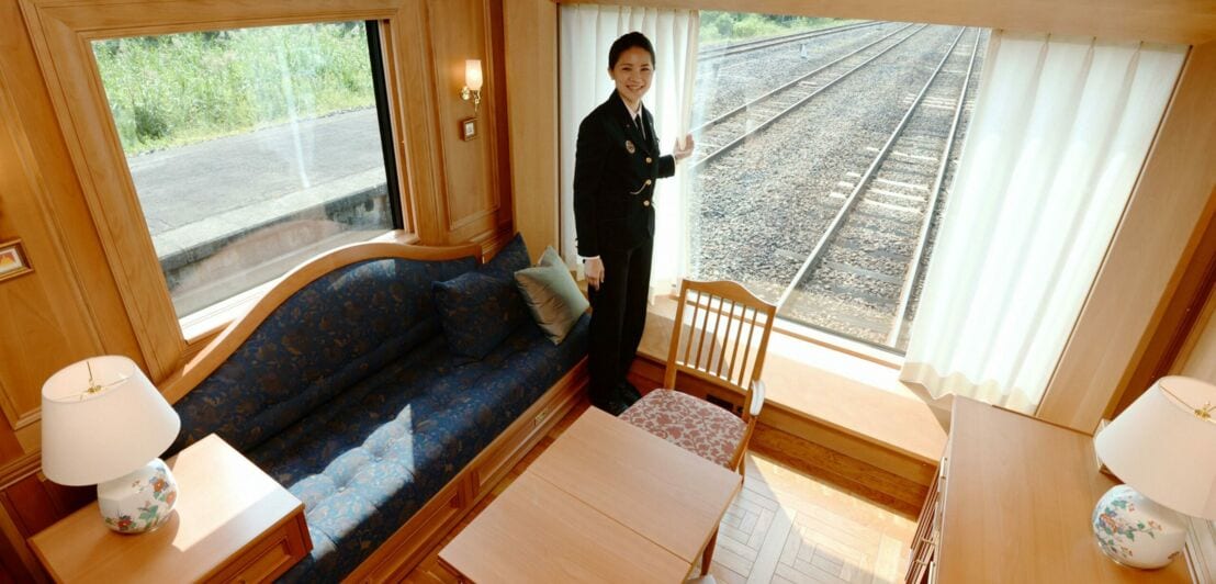 Eine Frau in Uniform steht an einem Panoramafenster in einer Suite mit Holzverkleidungen in einem Abteil am Ende des Zuges