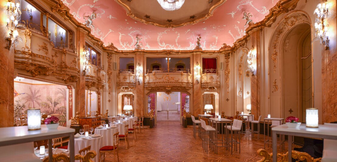 Ein Innenraum eines Ballsaales mit Tischen und Stühlen und einer beleuchteten Decke