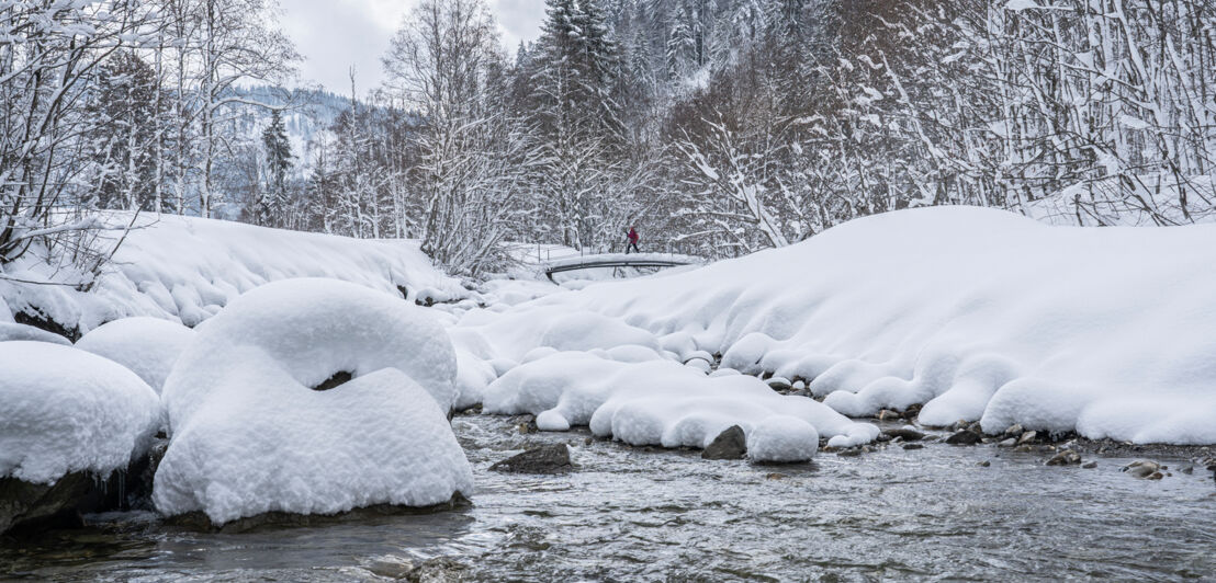 Eine Person spaziert in einer Winterlandschaft über einen schneebedeckten Fluss