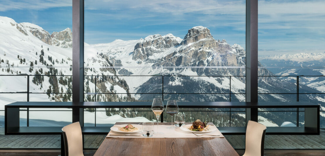 Ein elegant gedeckter Tisch mit zwei Stühlen vor einem Panoramafenster mit Sicht auf ein schneebedecktes Bergmassiv