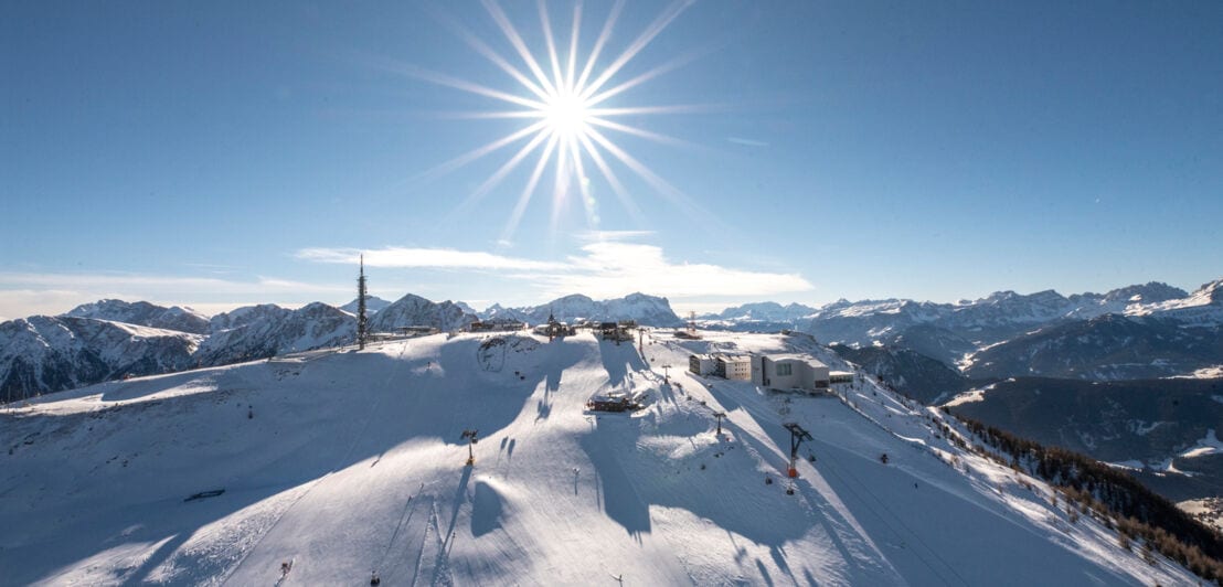 Panoramaaufnahme eines Skigebiets auf einem Gipfel mit Rundumblick über die schneebedeckte Berglandschaften bei Sonnenschein