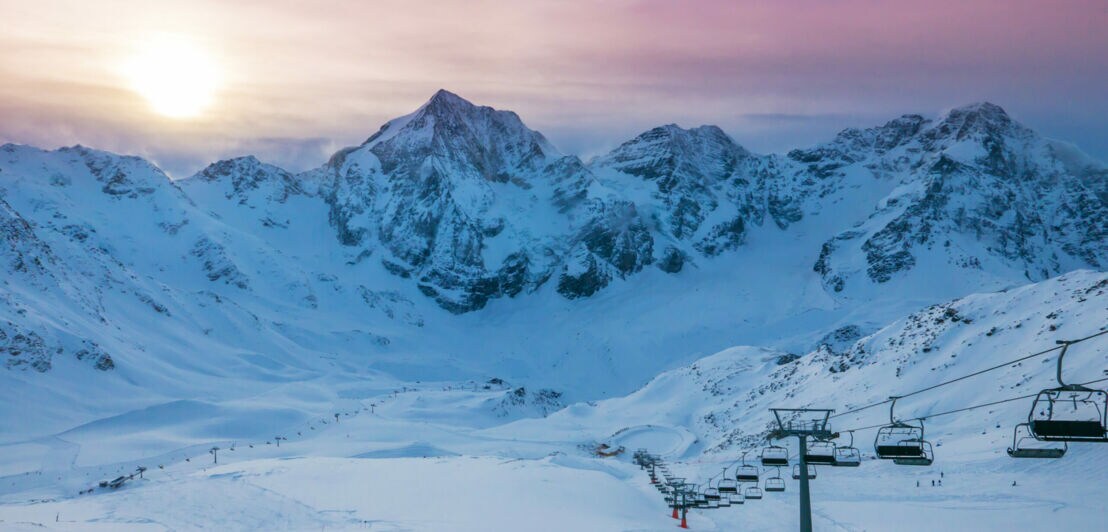 Leeres Skigebiet mit Sessellift vor Bergmassiv bei Sonnenaufgang