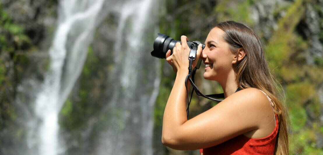 Eine junge Frau fotografiert einen Wasserfall.