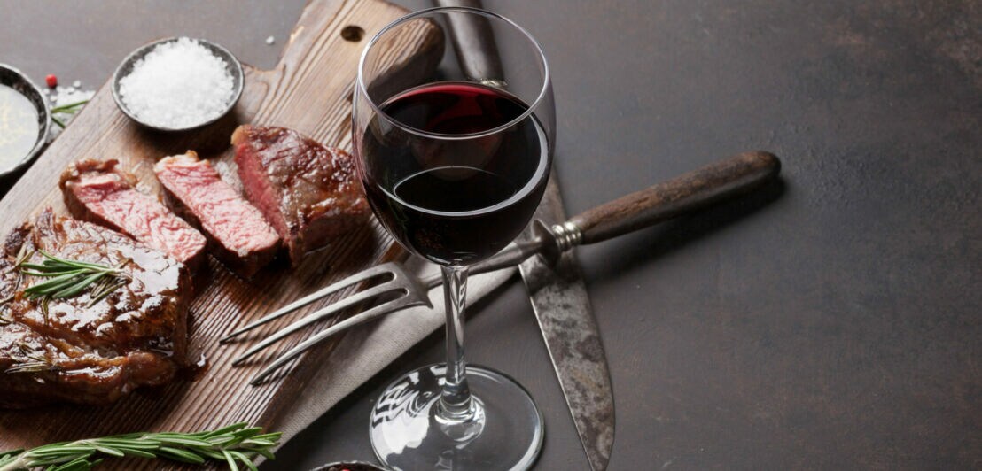 Ein Glas Rotwein neben einem Brett mit Fleisch.