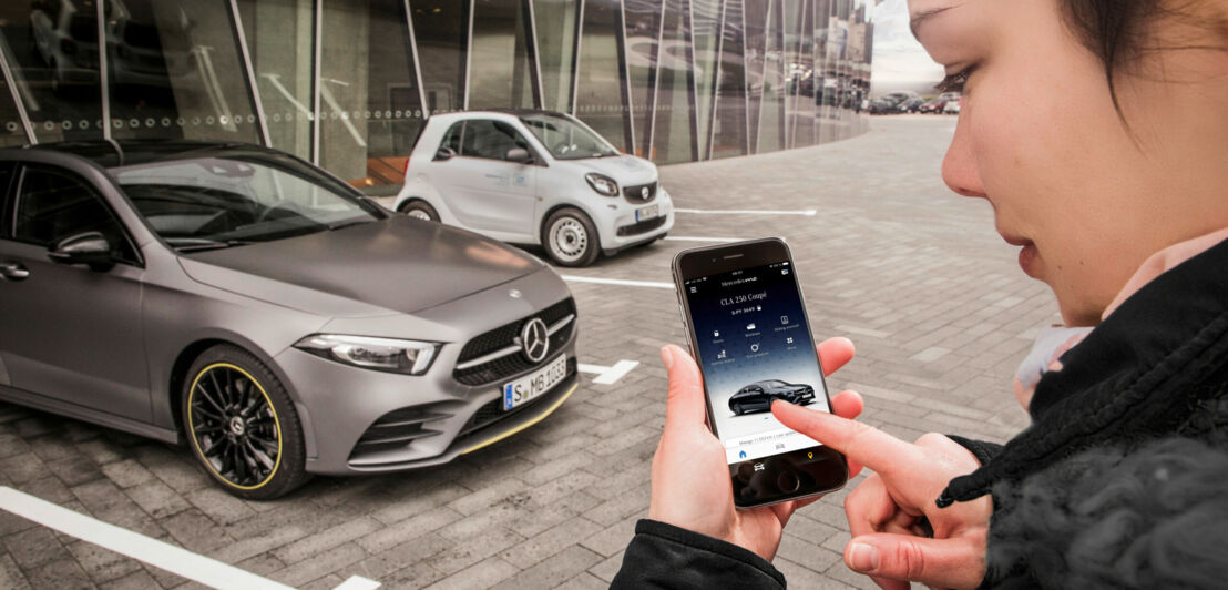 Eine Frau steht mit ihrem Smartphone vor einem Mercedes.