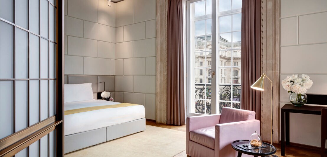 Eine moderne, luxuriöse Hotelsuite in Pastelltönen und einem Jugendstilbalkon inklusive Panoramafenster und Blick ins Stadtzentrum