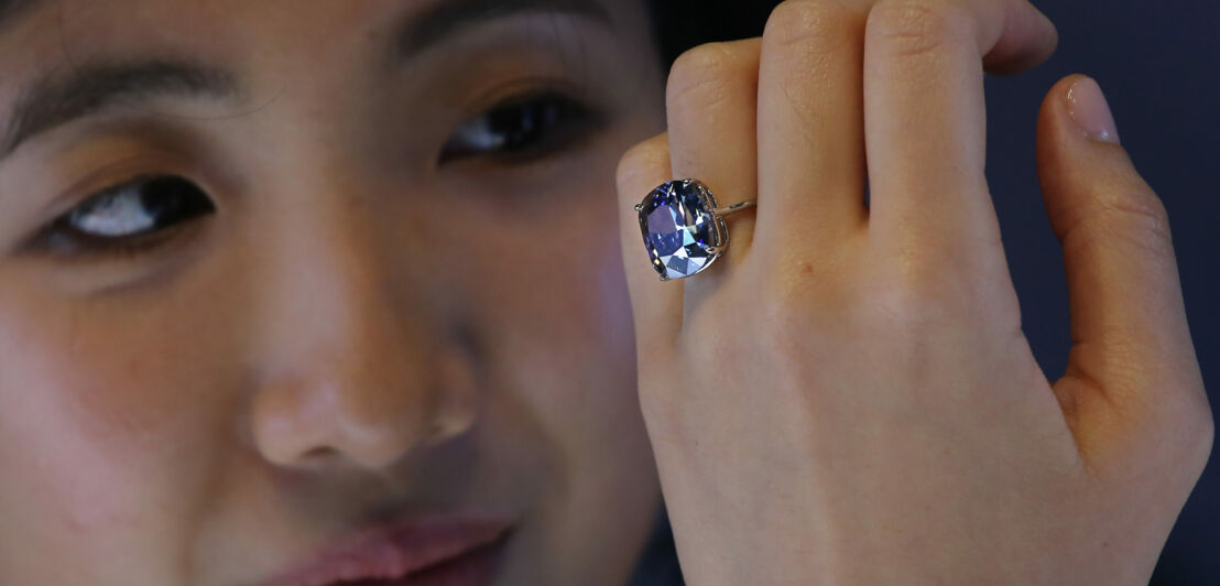 Eine Frau blickt auf einen blauen Diamantring an ihrer Hand