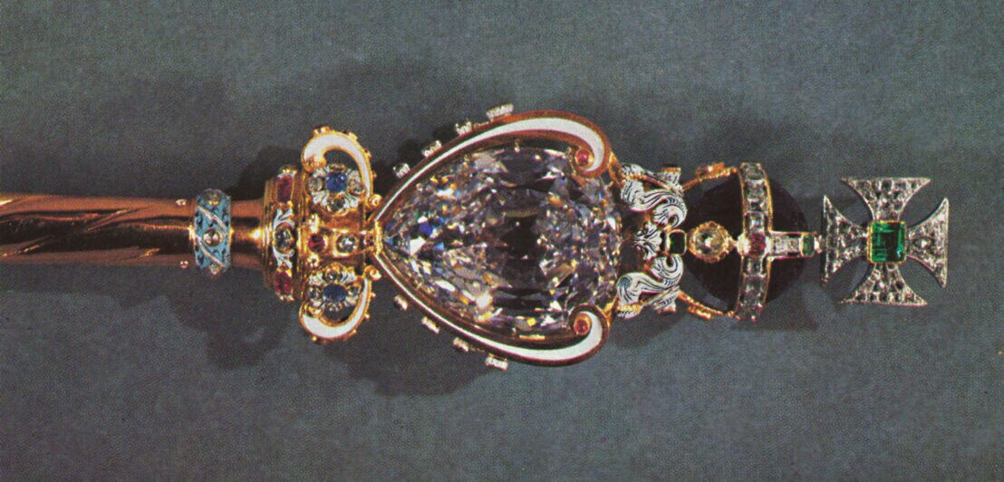 Ein goldenes Königszepter mit Kreuz, besetzt mit Edelsteinen und einem großen Diamanten