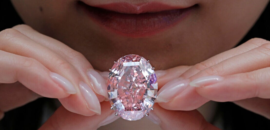 Ein großer, rosafarbener Diamant wird von zwei Händen gehalten