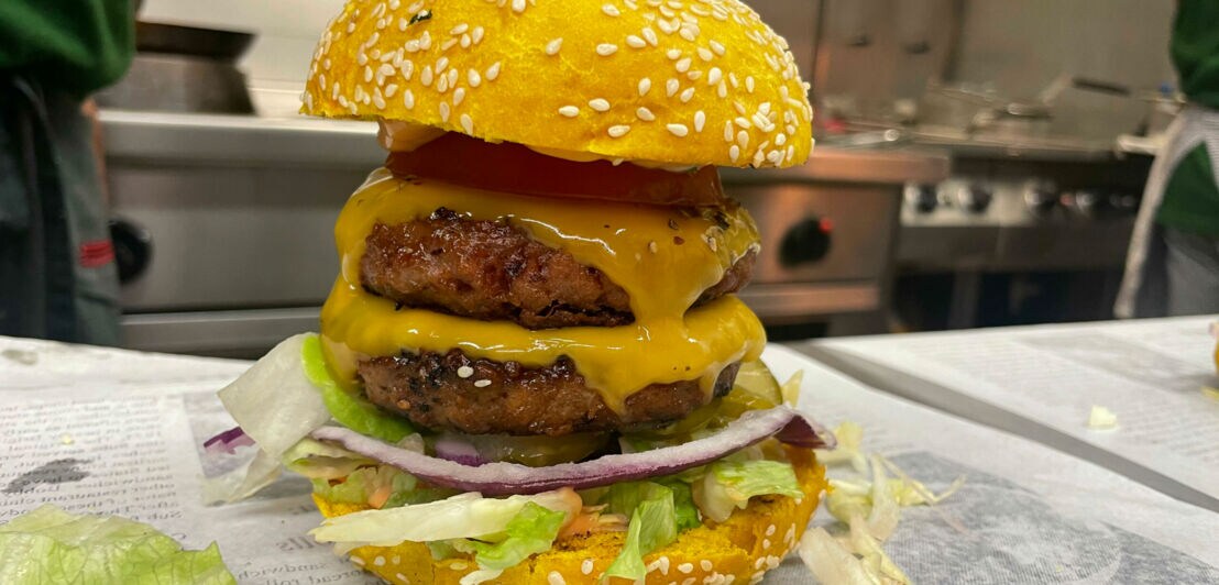 Nahaufnahme eines gestapelten, vegetarischen Cheeseburgers mit gelben Brötchenhälften in einer Küche
