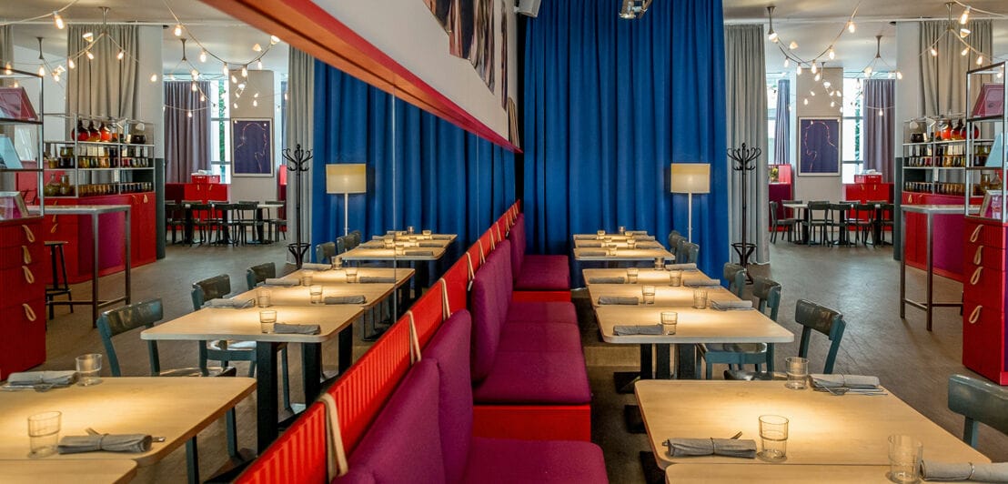 Ein modernes Restaurant im minimalistischen Design mit gedeckten Tischen und roten Bänken entlang einer Spiegelfront