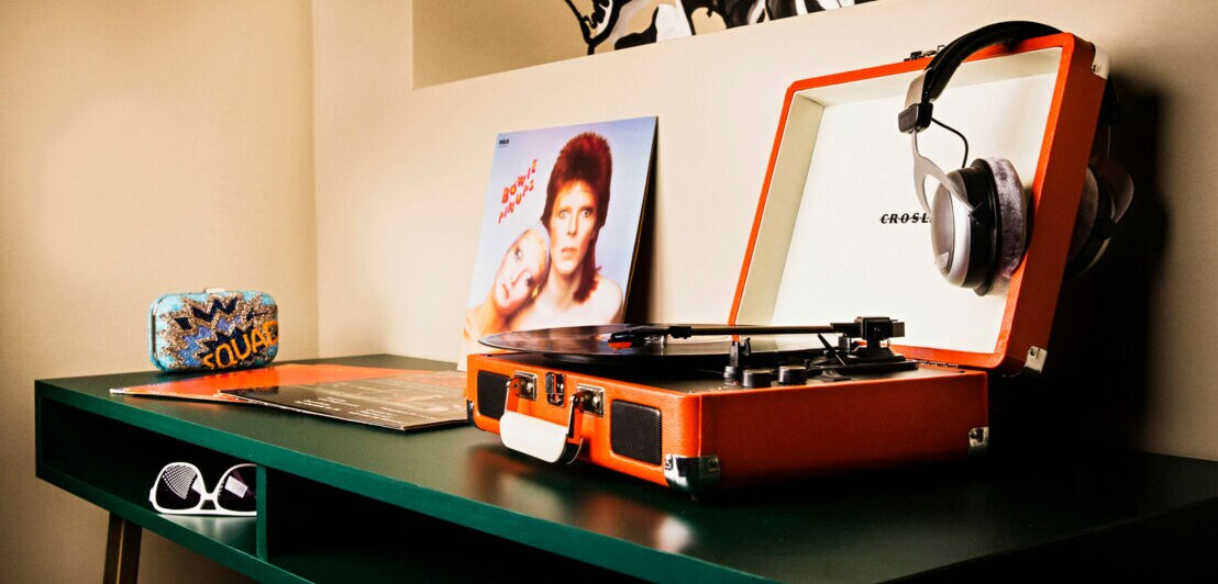 Ein Grüner Tisch mit portablem Plattenspieler und einer David Bowie Schallplatte danaben