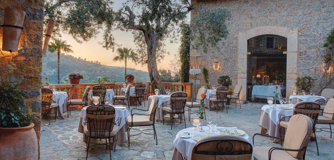 Eine mediterrane Terrasse mit Tischen, Stühlen und Bäumen in der Abendsonne