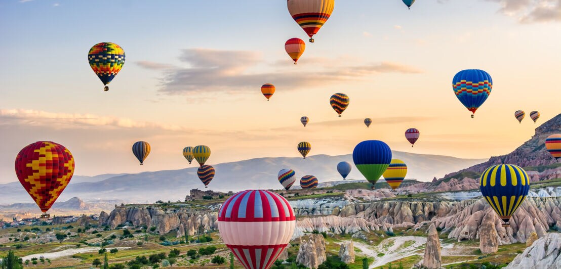 Bunte Heißluftballons über der kargen Landschaft von Kappadokien