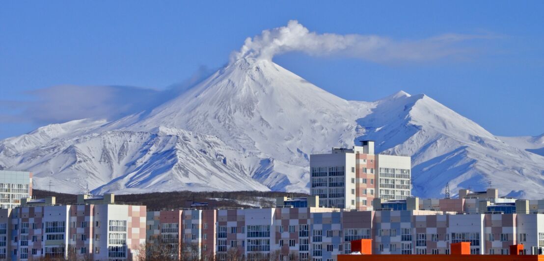 Eine Reihe Plattenhäuser der Stadt Petropawlowsk-Kamtschatski vor verschneitem Bergpanorama mit Vulkan