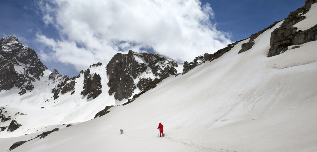 Ein Wanderer mit Hund läuft durch Tiefschnee im Gebirge