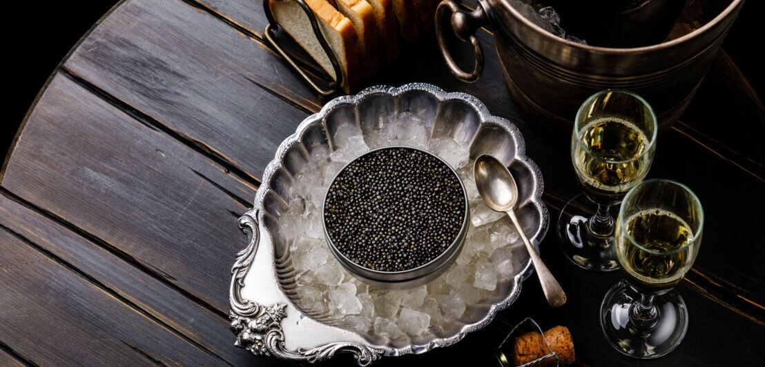 Kaviar in Silberschale auf Eis angerichtet, daneben Sektgläser und Toastbrot