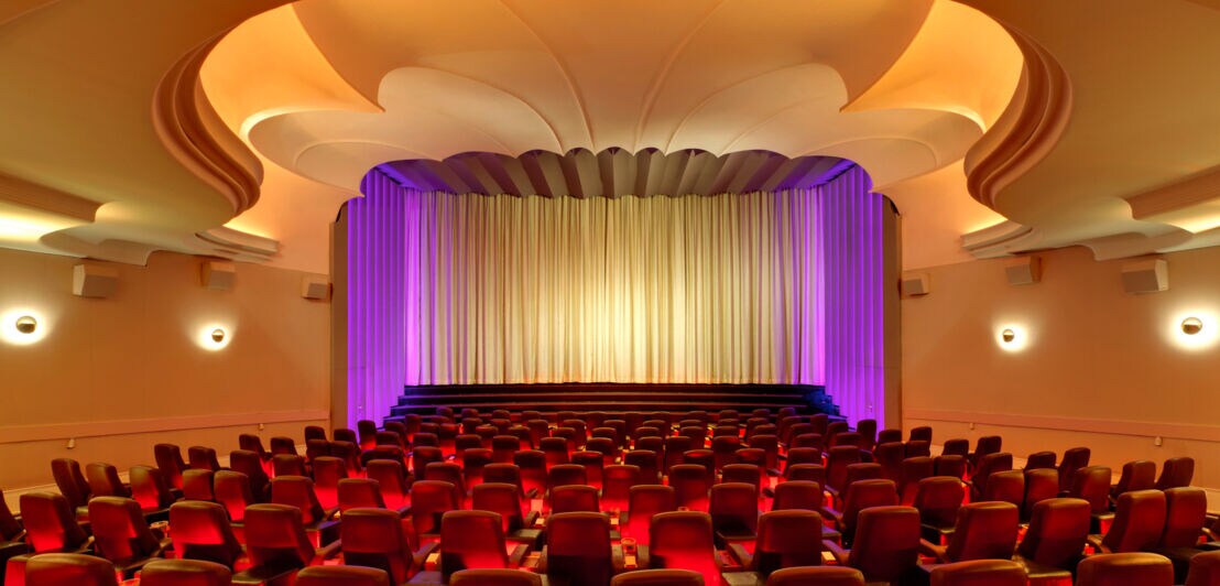 Beleuchteter Kinosaal mit roten Stühlen und Bühne